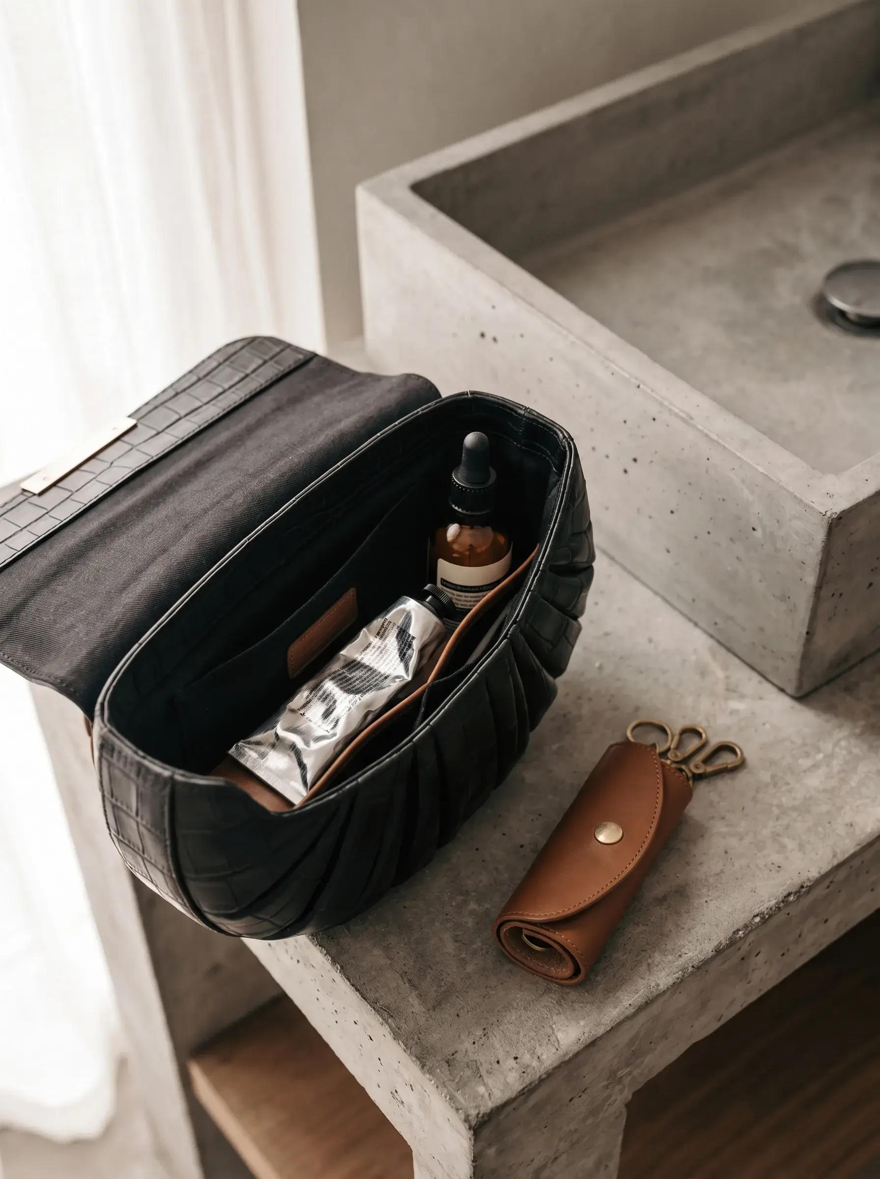 Sac noir ouvert contenant un organiseur, un tube métallique et un flacon brun