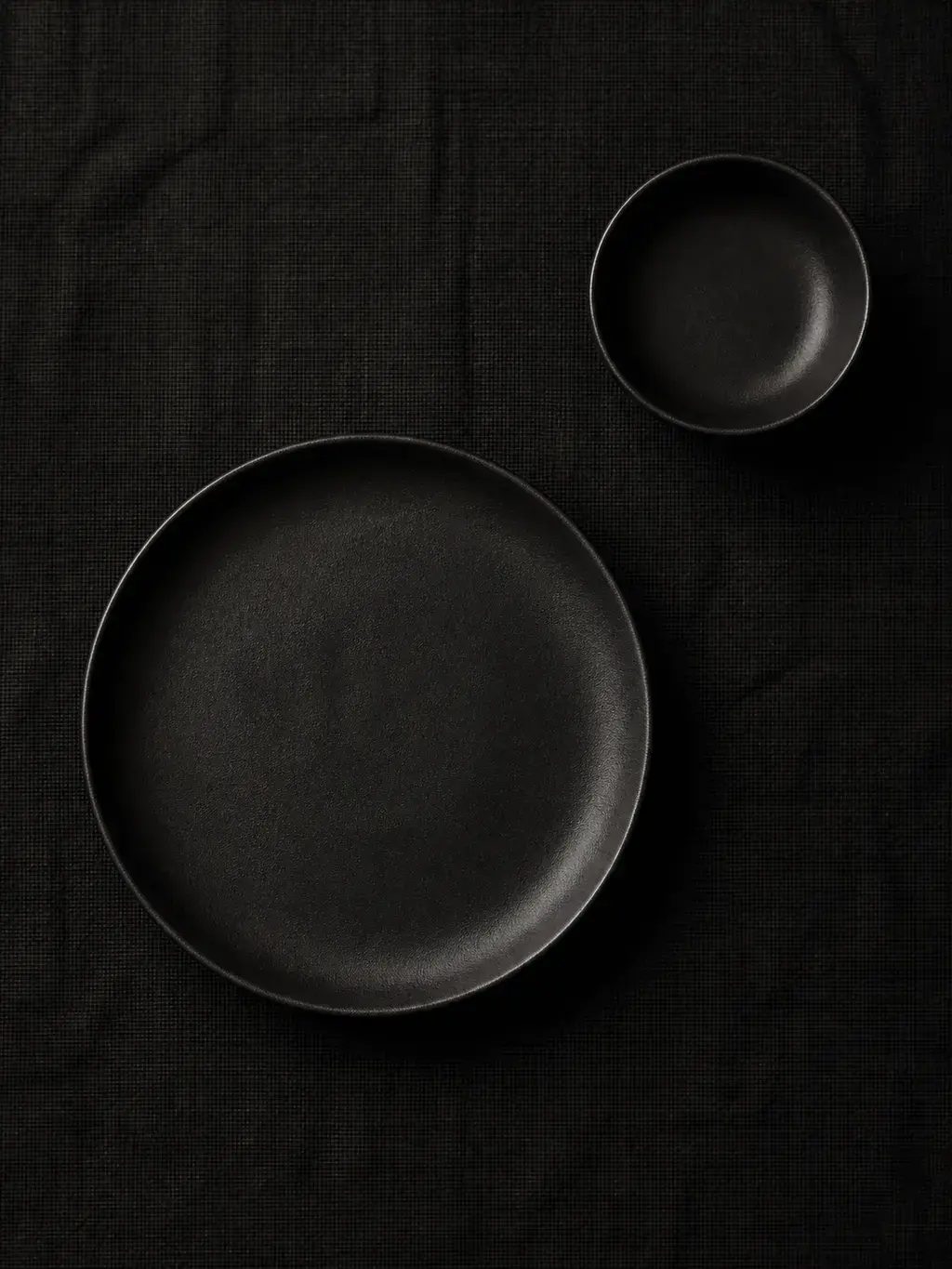 Assiette et bol en céramique noire sur nappe de lin noir
